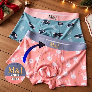 May include: Two pairs of boxer briefs. The top pair is teal with a pink waistband featuring the text M&J and a pattern of sleeping koalas and leaves. The bottom pair is pink with a grey waistband featuring the text M&J and a pattern of white rabbits and orange carrots.
