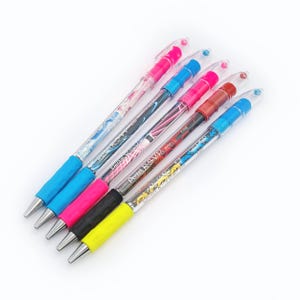 Puede incluir: Seis bolígrafos de colores con cuerpos transparentes y diferentes diseños de patrones. Los bolígrafos tienen tinta negra y están etiquetados como "Pentel R.S.V.P. Fine".