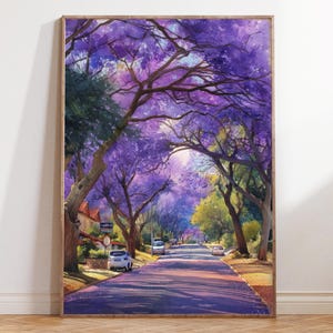 May include: A framed watercolor painting of a tree-lined street with purple flowering trees. The artwork depicts a sunny day with shadows cast on the road. Cars are parked along the street, and houses are visible in the background. The painting is in a wooden frame.