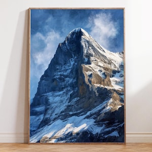 Puede incluir: Una impresión enmarcada de una cima montañosa cubierta de nieve contra un cielo azul con nubes. La montaña está representada con tonos de azul, blanco y marrón, y está enmarcada en madera.