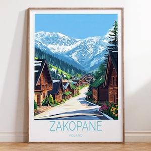 May include: A framed print of Zakopane, Poland, featuring a scenic mountain village. The artwork depicts wooden chalets with green roofs lining a road, with snow-capped mountains in the background under a clear blue sky. The word "ZAKOPANE" is printed in light blue.