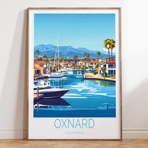 May include: A framed art print featuring a coastal scene of Oxnard, California. The artwork depicts a waterway with boats, houses, and palm trees under a clear blue sky. The word "OXNARD" is printed in a teal color at the bottom.