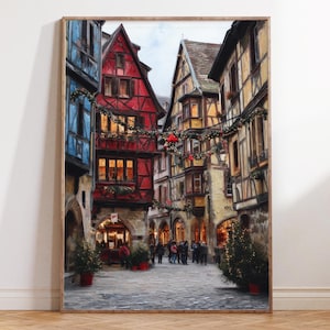 May include: A framed print depicting a European street scene. The buildings feature red, blue, and yellow facades with Christmas decorations. People are gathered in the cobblestone street, and small Christmas trees are in red pots.