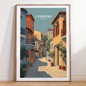 May include: A framed art print showing a street scene in Ioannina, Greece. The artwork features vibrant buildings in orange, blue, and yellow along a cobbled street. The print includes the text "Ioannina Greece" at the top.
