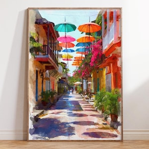 May include: A framed watercolor painting of a colorful street scene. The artwork depicts a narrow street lined with buildings in shades of orange, yellow, and pink. Overhead, vibrant umbrellas in various colors are suspended, casting shadows on the cobblestone street.