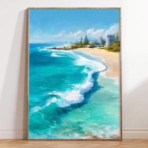 May include: A framed art print of a coastal scene. The artwork depicts a turquoise ocean with white waves crashing onto a sandy beach. Buildings and a blue sky with clouds are visible in the background. The frame is a light brown color.