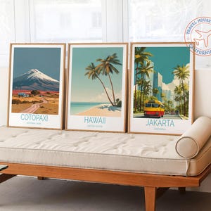May include: Three framed travel art prints featuring scenic destinations: Cotopaxi National Park, Hawaii, and Jakarta, Indonesia. Each print has a wooden frame and showcases vibrant illustrations of landscapes and landmarks. The prints are displayed on a wooden bench.