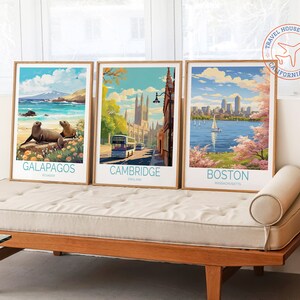 K&ouml;nnte beinhalten: Drei Vintage-Reiseposter mit Holzrahmen. Die Poster zeigen Bilder von Galapagos, Cambridge und Boston. Die Poster werden auf einem hellbraunen Sofa mit einem wei&szlig;en Kissen ausgestellt.