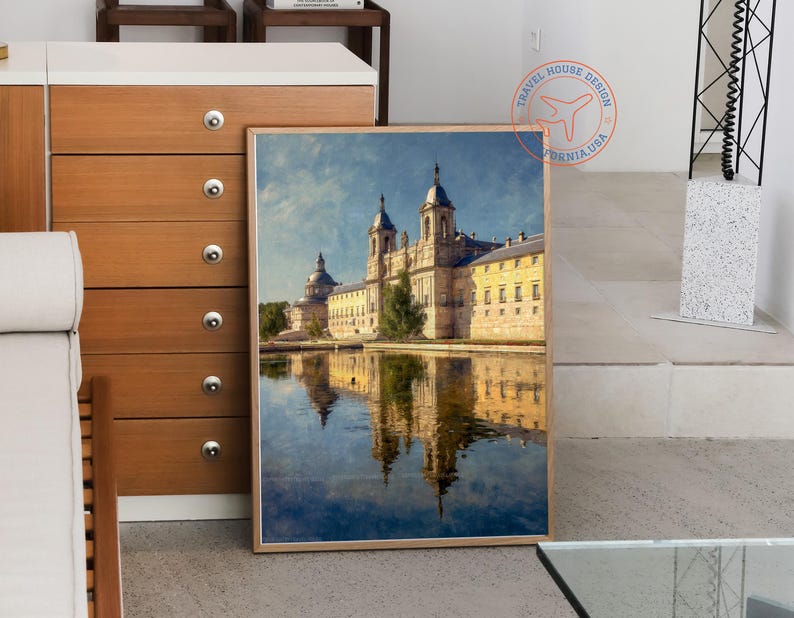 May include: A framed print of a grand building reflected in water. The building has multiple domes and towers, with a yellow facade and a blue sky background. The print is in a light brown frame.