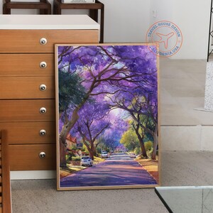 May include: A framed watercolor painting depicts a tree-lined street with purple flowering trees. The artwork showcases a road leading into the distance, with cars parked along the sides. The painting has a warm, inviting color palette.