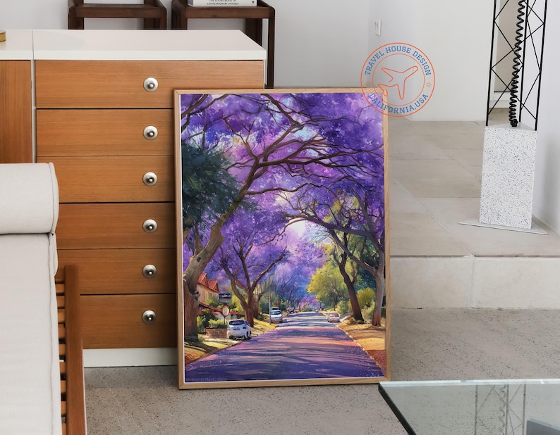 May include: A framed watercolor painting depicts a tree-lined street with purple flowering trees. The artwork showcases a road leading into the distance, with cars parked along the sides. The painting has a warm, inviting color palette.