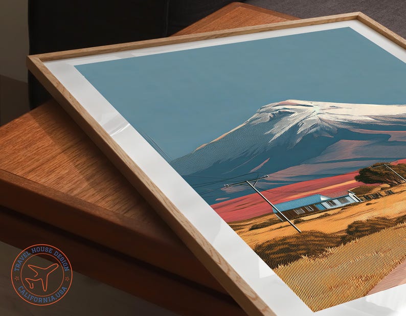 May include: Framed art print featuring a mountain landscape with a snow-capped peak, a blue sky, and a house. The artwork has a white border and a natural wood frame. The print has a Travel House Design California USA logo.