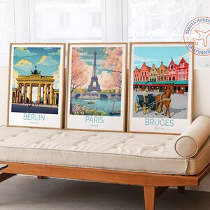 May include: Three framed travel posters with vintage-style illustrations of iconic landmarks. The posters feature the Brandenburg Gate in Berlin, the Eiffel Tower in Paris, and the Markt in Bruges. Each poster has the city name and country printed below the image.