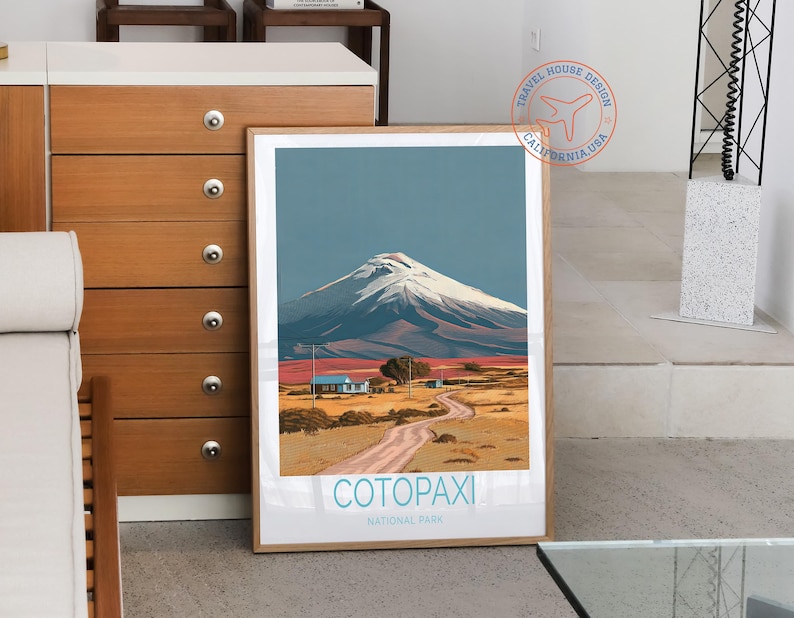 May include: A framed art print featuring a landscape scene of Cotopaxi National Park. The artwork depicts a snow-capped mountain under a blue sky, with a dirt road leading to small buildings. The text "Cotopaxi National Park" is at the bottom.