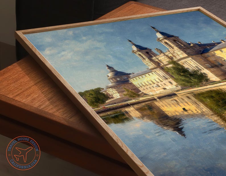 May include: A framed print of a European palace reflected in water. The artwork features a light wooden frame and a detailed depiction of the building's architecture, with a blue sky and water. The Travel House Design logo is visible in the lower left corner.