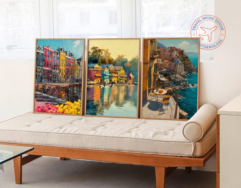 Op de afbeelding: Drie ingelijste kunstdrukken met Europese stadsgezichten. Het kunstwerk toont kleurrijke gebouwen, waterreflecties en kustgezichten. De prints worden tentoongesteld op een houten daybed. Het Travel House Design-logo staat rechtsboven.
