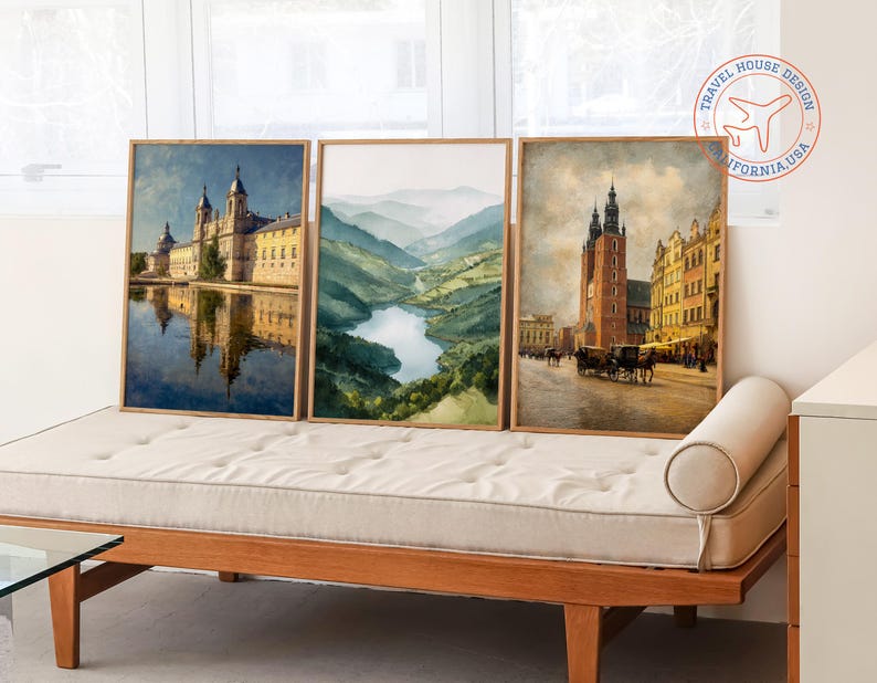 May include: Three framed watercolor prints featuring European landscapes. The prints depict a monastery reflected in water, a mountain valley with a river, and a city scene with a tall building and horse-drawn carriages. The frames are made of light-colored wood.