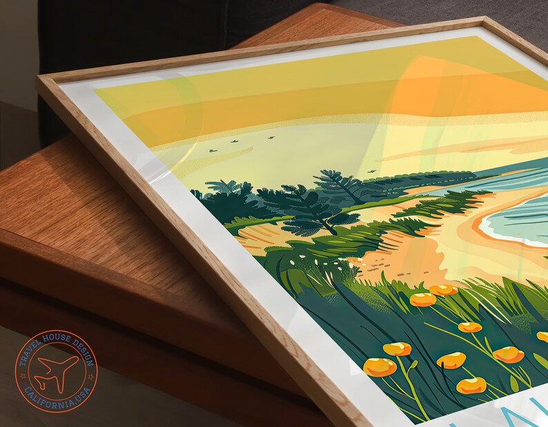 May include: A colorful illustration of a beach scene with a sandy shore, blue water, and green trees. The sky is a gradient of yellow and orange, suggesting a sunset. The image is framed in a light wood frame.
