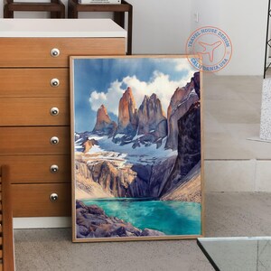 K&ouml;nnte beinhalten: Ein gerahmter Aquarelldruck einer Berglandschaft. Das Kunstwerk zeigt hoch aufragende, zerkl&uuml;ftete Gipfel mit schneebedeckten Gipfeln, einen t&uuml;rkisfarbenen See und einen bew&ouml;lkten Himmel. Der Druck ist in einem Naturholzrahmen.