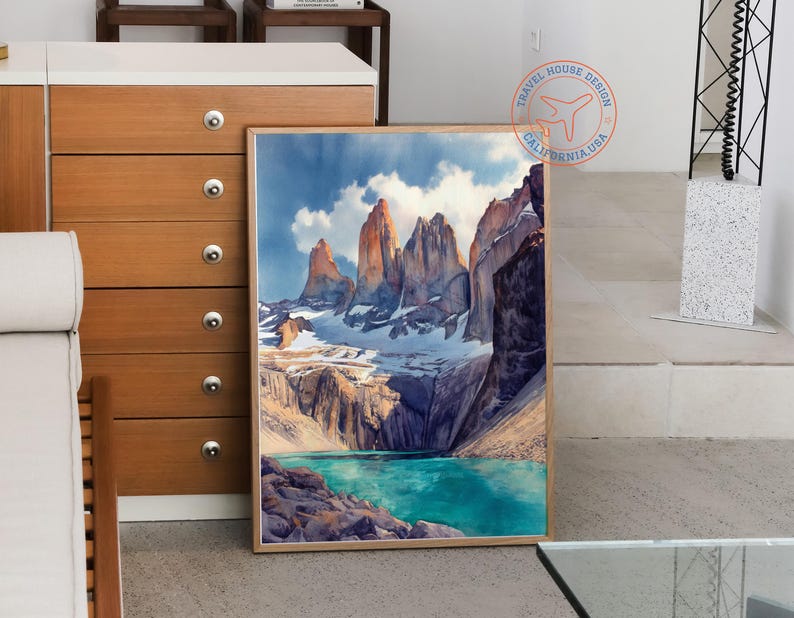 K&ouml;nnte beinhalten: Ein gerahmter Aquarelldruck einer Berglandschaft. Das Kunstwerk zeigt hoch aufragende, zerkl&uuml;ftete Gipfel mit schneebedeckten Gipfeln, einen t&uuml;rkisfarbenen See und einen bew&ouml;lkten Himmel. Der Druck ist in einem Naturholzrahmen.