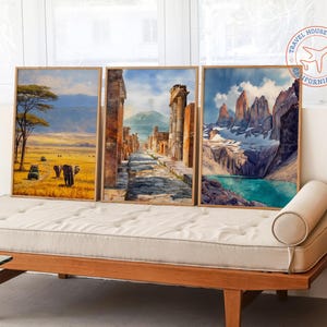 K&ouml;nnte beinhalten: Drei gerahmte Landschaftskunst-Drucke. Die Drucke zeigen eine Savannenszene mit Elefanten, eine antike Stadt und eine Bergkette mit einem See. Die Rahmen sind hellbraun. Die Kunst wird auf einem h&ouml;lzernen Tagesbett ausgestellt.
