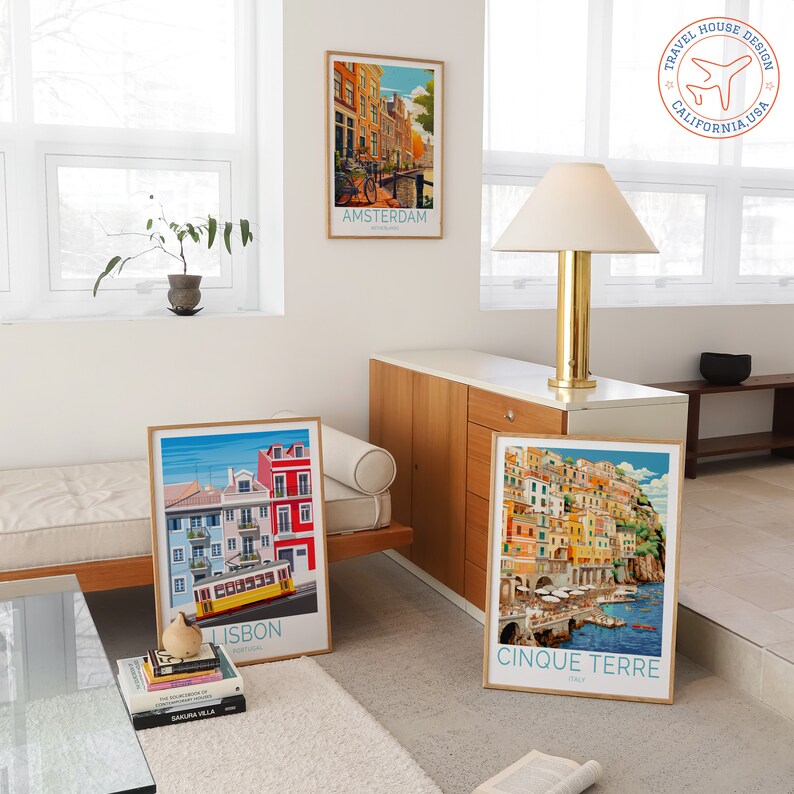 May include: Four framed travel posters with colourful illustrations of Amsterdam, Lisbon, Cinque Terre, and a plane with the text "Travel House Design California USA".