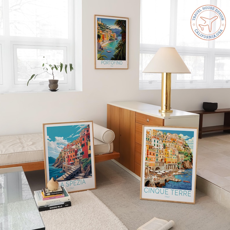 May include: Three framed travel posters featuring Italian coastal scenes. One poster displays "Portofino", another "La Spezia", and the third "Cinque Terre". The posters have a vintage travel aesthetic with vibrant colors and detailed illustrations.