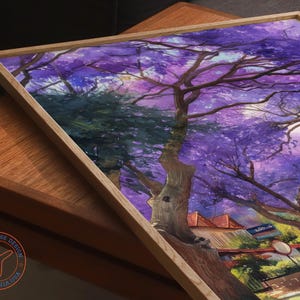 May include: A framed art print featuring a vibrant watercolor painting of a tree with purple blossoms. The artwork is set against a backdrop of buildings and a street scene, with a light-colored wooden frame. The Travel House Design logo is visible.