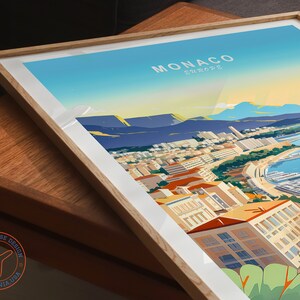 May include: Framed art print of Monaco, Europe, featuring a vibrant illustration of the city's coastline, buildings, and harbor. The print has a light wood frame and white matting. The artwork is signed by Travel House Design, California, USA.