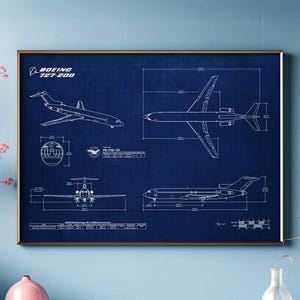 May include: A framed blueprint of a Boeing 727-200 aircraft. The detailed technical drawings are in white against a dark blue background. The frame is a warm brown color. The top left corner of the image has the text "BOEING 727-200".