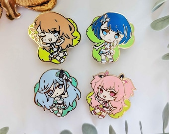 May include: Four enamel pins featuring anime-style characters with colourful hair and outfits. The pins are set against a white background with green leaves.
