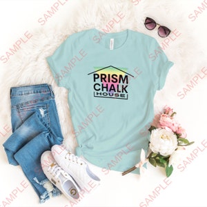 May include: A light blue t-shirt with a graphic of a house with the text "Prism Chalk House" in black letters. The house is filled with a rainbow gradient.