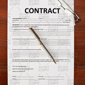 May include: A standard legal contract form with the word "CONTRACT" printed at the top. The form includes sections for the parties involved, witnesses, and the date of the agreement. A silver pen is lying on the form.