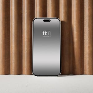 以下が含まれることがあります： 白い表面に置かれた、黒い画面に11:11と日付が「日曜日、1月1日」と表示されている銀色のスマートフォン。スマートフォンの後ろには、茶色の木製の壁がある。