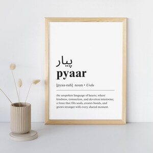 May include: A framed print with a black and white definition of the Urdu word "pyaar" which means love. The definition reads: "the unspoken language of hearts, where kindness, connection, and devotion intertwine; a force that fills souls, creates bonds, and grows stronger with every shared moment."