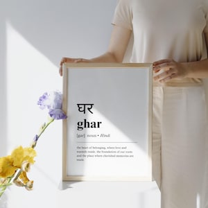 May include: A framed print with a white background and black text. The text reads "घर ghar [gar] noun Hindi the heart of belonging, where love and warmth reside, the foundation of our roots and the place where cherished memories are made."