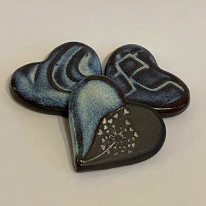 May include: Three ceramic heart-shaped ornaments in shades of blue and brown. One heart features a white dandelion design.