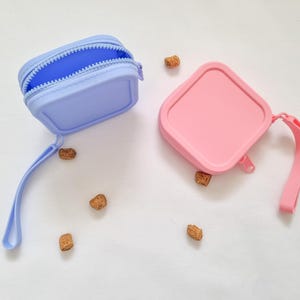 May include: Two small silicone pouches with zipper closures and attached straps. One pouch is light blue and the other is pink.
