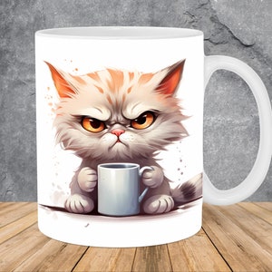 Op de afbeelding: Witte keramische mok met een cartoon afbeelding van een chagrijnige kat die een witte mok vasthoudt. De kat heeft oranje en witte vacht en gele ogen.
