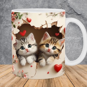 May include: White ceramic mug with a design of two kittens peeking through a torn piece of paper with red hearts. The kittens are looking at the viewer with big, green eyes.