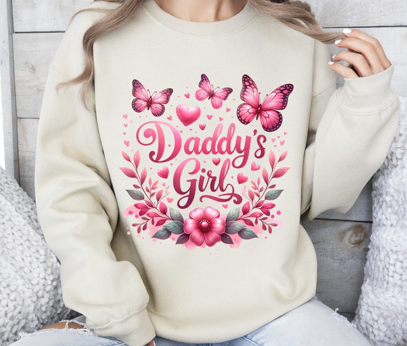 May include: A cream-colored sweatshirt with a pink floral design and the text "Daddy's Girl". The design includes butterflies, hearts, and leaves.