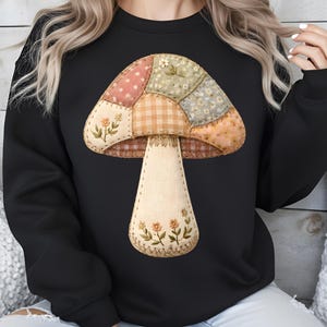 Puede incluir: Sudadera negra con un diseño de hongo colorido. El hongo tiene un diseño de patchwork con patrones florales y de cuadros en tonos rosa, verde y beige. El tallo es de color crema con detalles florales.