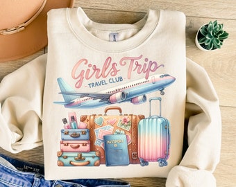 Peut inclure: Un sweat-shirt beige avec un motif graphique d'un avion, des bagages et un passeport. Le texte "Girls Trip - Travel Club" est imprimé sur le sweat-shirt.