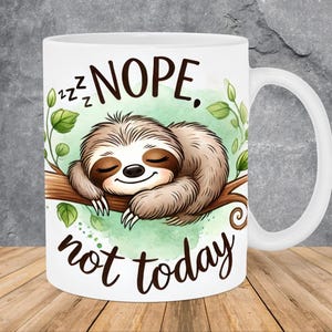 May include: White ceramic mug with a cartoon sloth sleeping on a branch. The mug has green watercolor leaves and the text "zzz NOPE. not today".