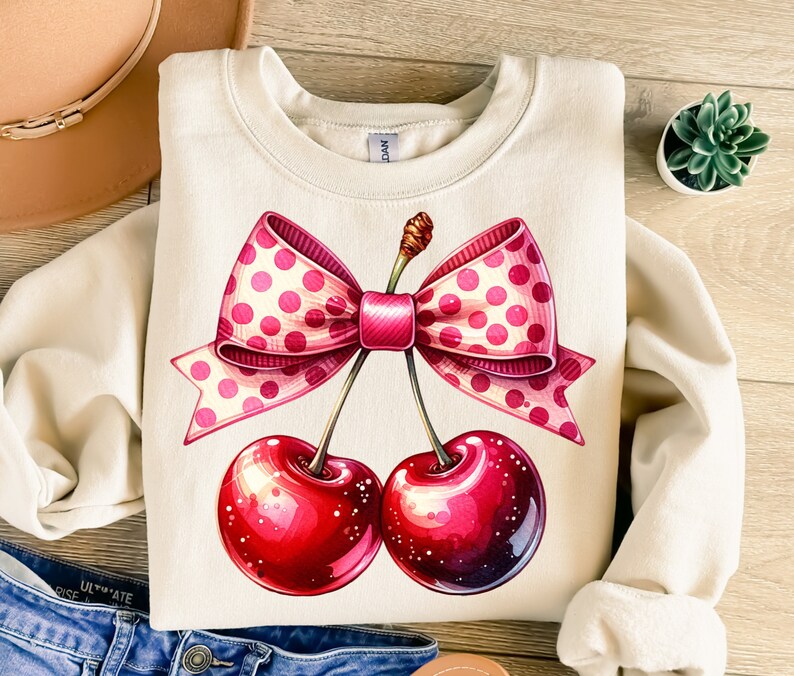 May include: A cream-colored sweatshirt with a pink and white polka dot bow and two red cherries. The cherries have stems and leaves.