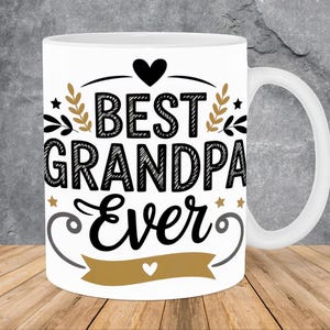 Peut inclure: Mug en céramique blanche avec l'inscription "BEST GRANDPA Ever" en noir, avec des éléments décoratifs dorés et noirs. La tasse a une anse blanche et est posée sur une surface en bois.