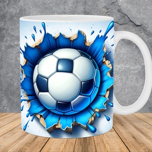 Könnte beinhalten: Weiße Keramiktasse mit einem blauen und weißen Fußball-Motiv. Der Fußball ist von blauen Farbstichen umgeben und scheint eine weiße Oberfläche zu durchbrechen.