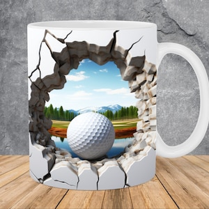 May include: White ceramic mug with a golf ball breaking through a cracked wall design. The scene behind the wall shows a golf course with a lake and mountains in the background.