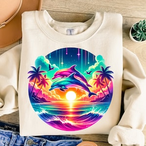 May include: A white sweatshirt with a colorful graphic print of two dolphins jumping over a sunset ocean scene. The graphic includes palm trees, a starry sky, and a rainbow-colored wave.