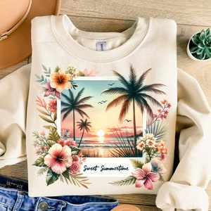 May include: A beige sweatshirt with a graphic print of a sunset beach scene with palm trees and flowers. The text "Sweet Summertime" is printed below the image.